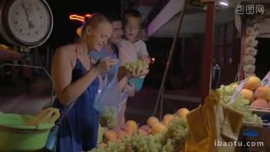 一家三口在深夜的市场上买水果，妈妈拿着葡萄和桃子